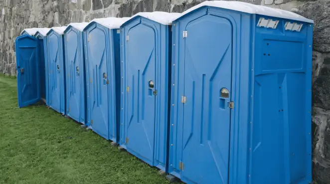 Row of blue portable toilets lined up on grass against a stone wall for event sanitation in Honolulu, HI