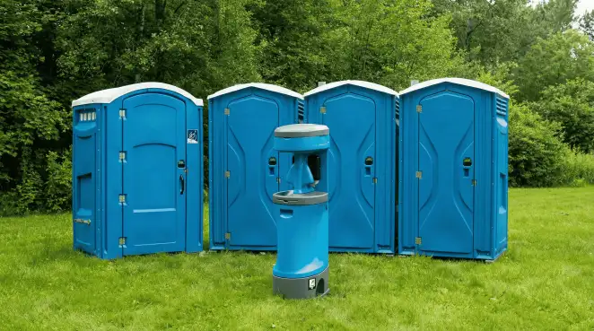 Four blue portable toilets and a matching hand washing station on grass near trees, a common sight at local outdoor events in Honolulu, HI