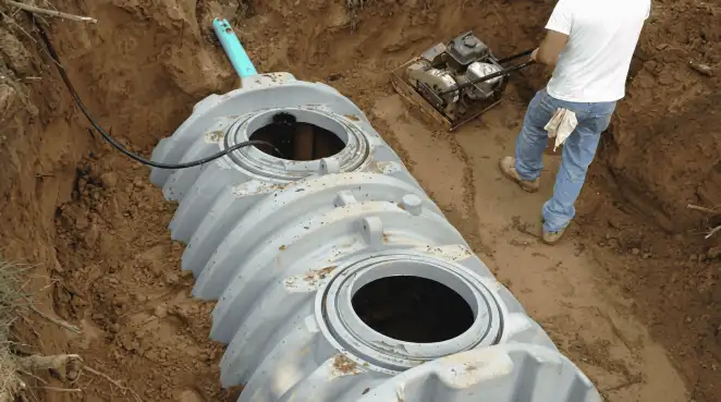 Septic tank installation showing a technician compacting soil around a new poly septic tank in an excavation pit in Honolulu, HI